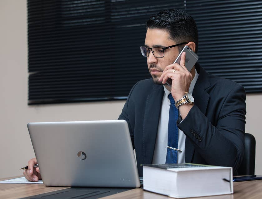 A General Counsel in his office in front of his laptop working on some legal documents while talking on the phone.