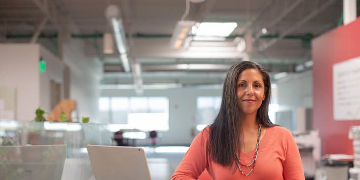 Female General Manager standing inside the office with an open laptop beside her