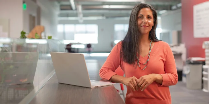 A female general manager standing inside an office with an open laptop beside her.