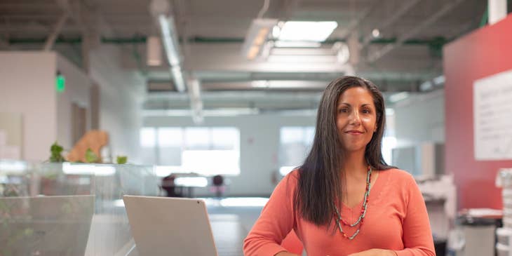 Female General Manager standing inside the office with an open laptop beside her