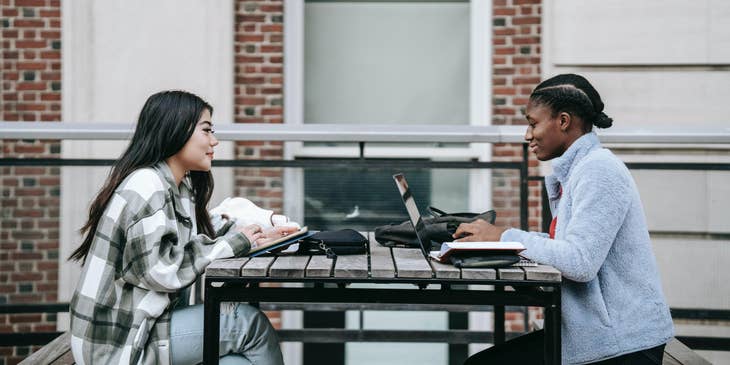 A graduate trainee takes notes while talking to a coworker.