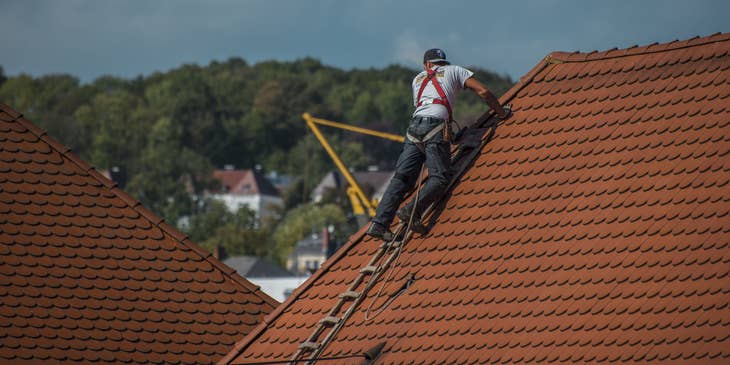 Gutter installer on a house roof with ladder and tools