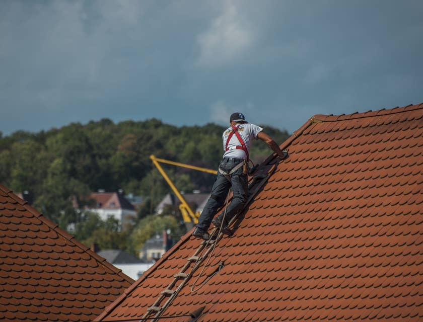 Gutter installer on a house roof with ladder and tools