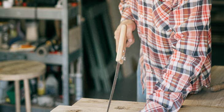 Handyman using a handsaw on wooden boards.