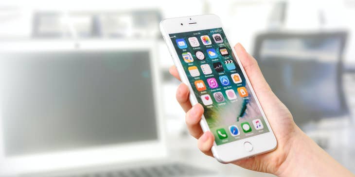 A person holding a phone with app icons and a laptop in the background.