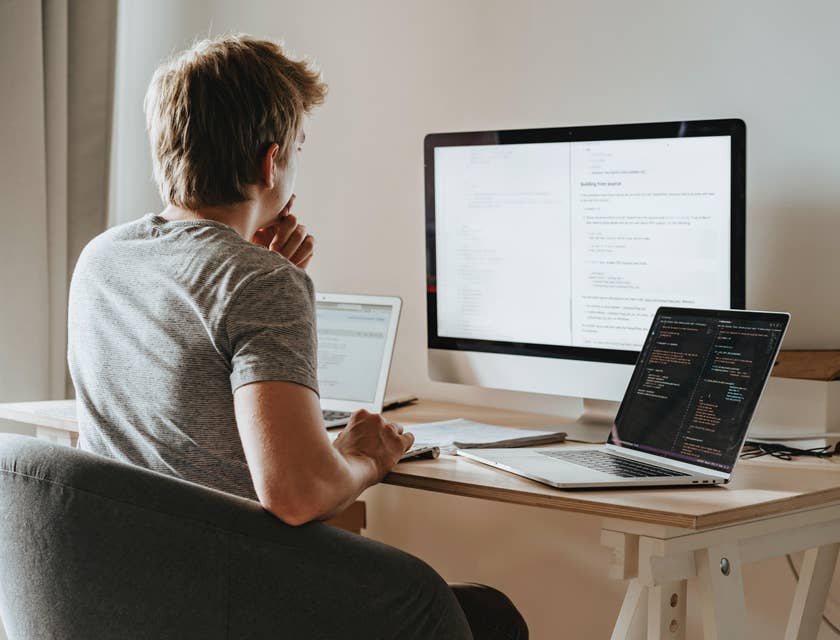 A man working on a coding program with three computers.