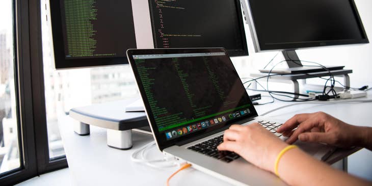 A programmer working on a program with a laptop and two computer screens.