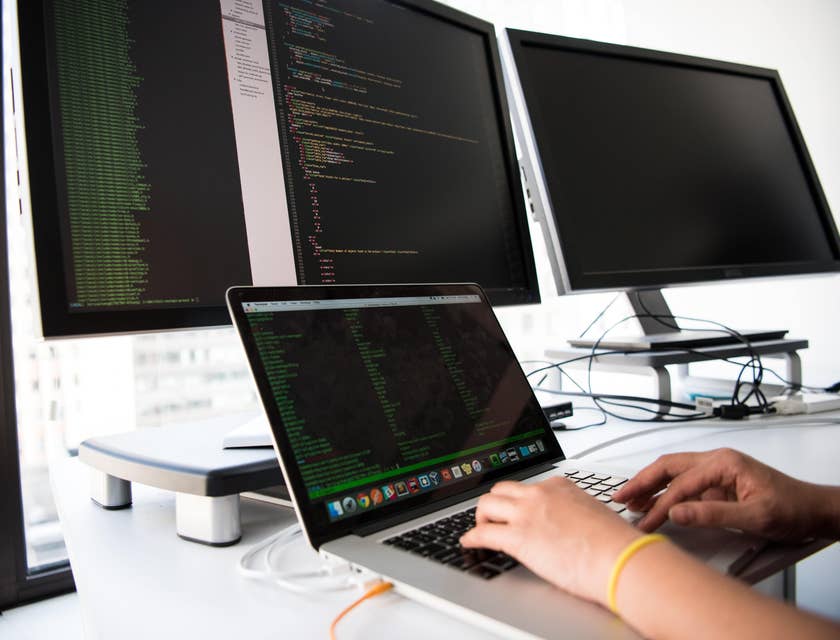 A programmer working on a program with a laptop and two computer screens.
