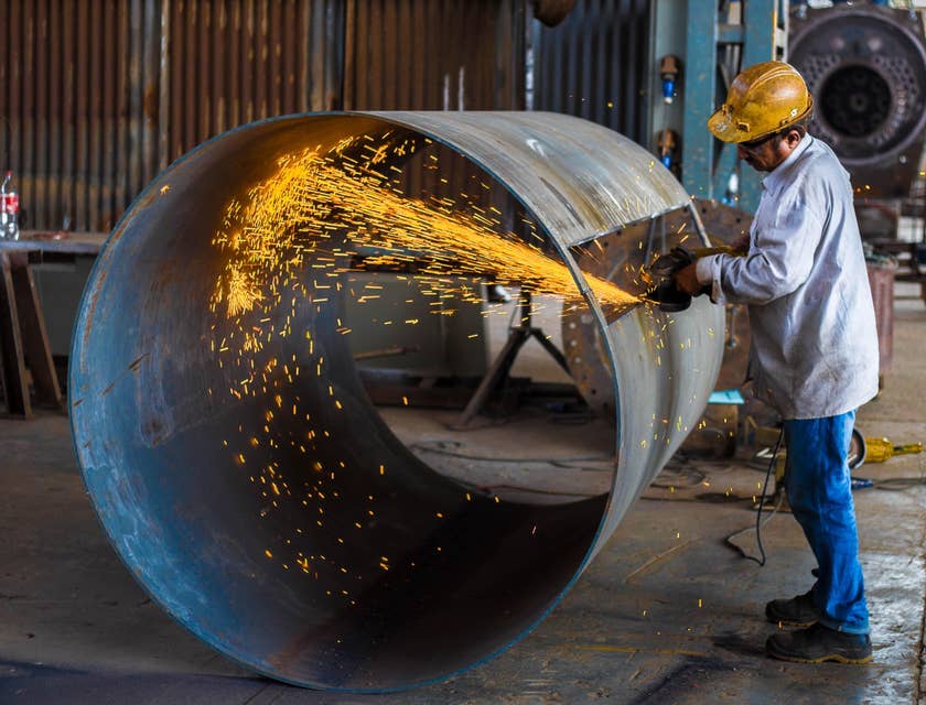 welder with helmet working on large metal cylinder