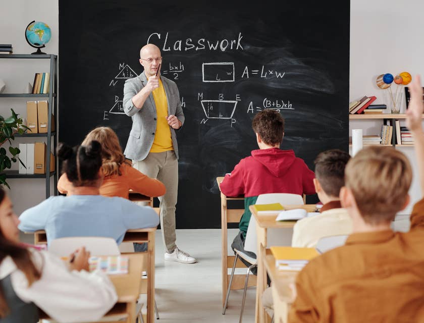 A math teacher standing near a blackboard and teaching a class.