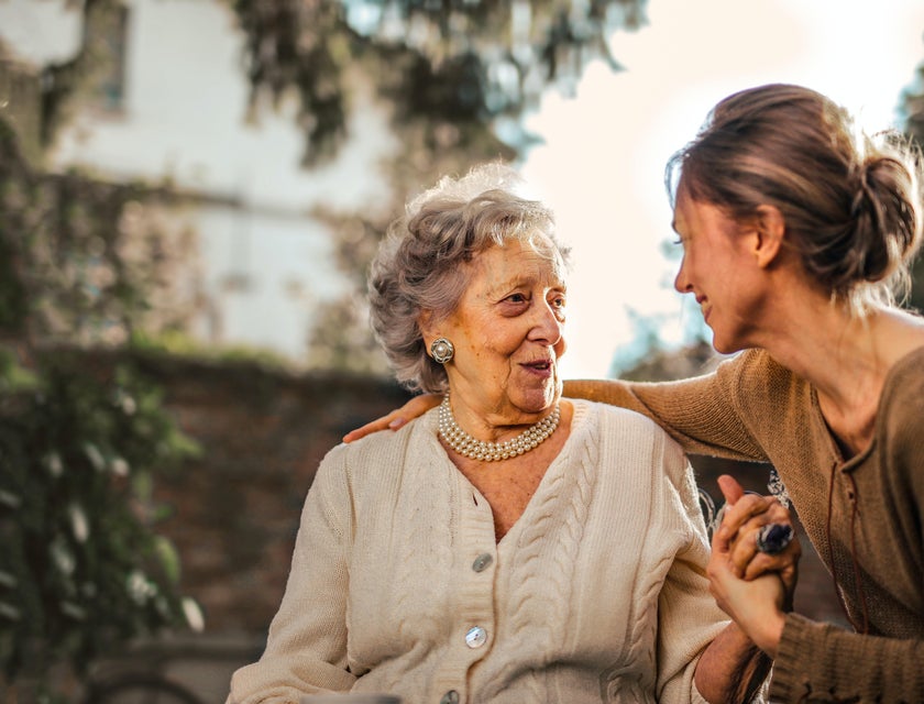 smiling home health aide holding the hand of an elderly woman
