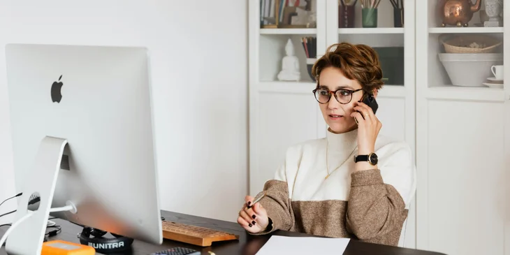A female HR director looking at her computer and holding a pen while talking on the phone.
