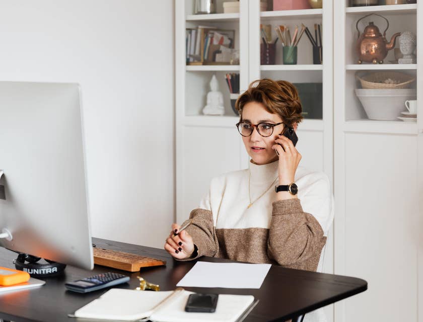 A female HR director looking at her computer and holding a pen while talking on the phone.