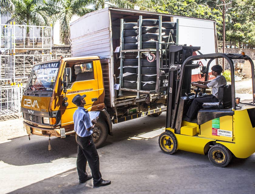 An Industrial Truck and Tractor Operator driving a tractor loading tires and about to transport items inside the warehouse.