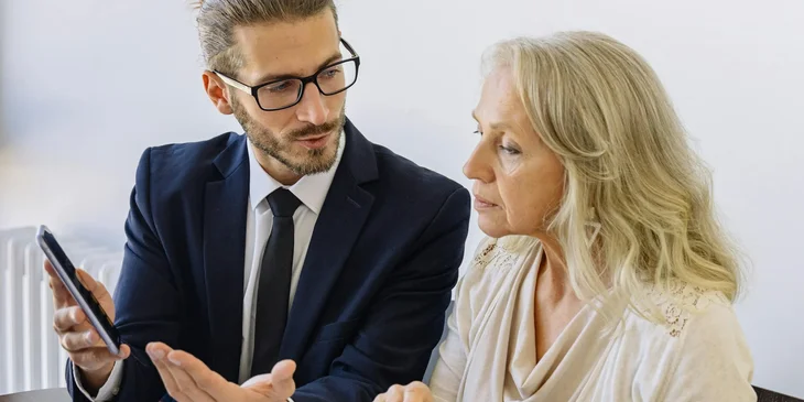 An insurance consultant in a black suit sitting and discussing with a client in an office setting.