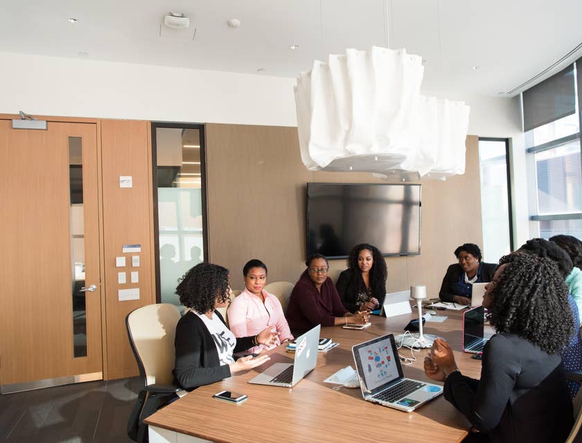 A Female Insurance Sales Manager sitting and discussing with her co employees around a wooden table.