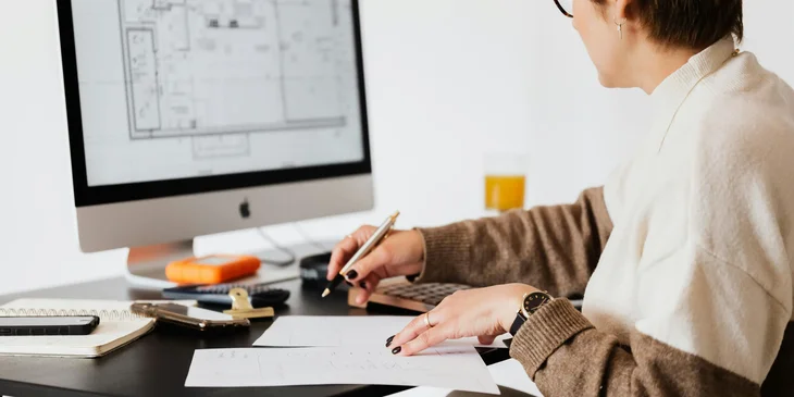 An interior designer sketching new design plans while comparing on her computer.