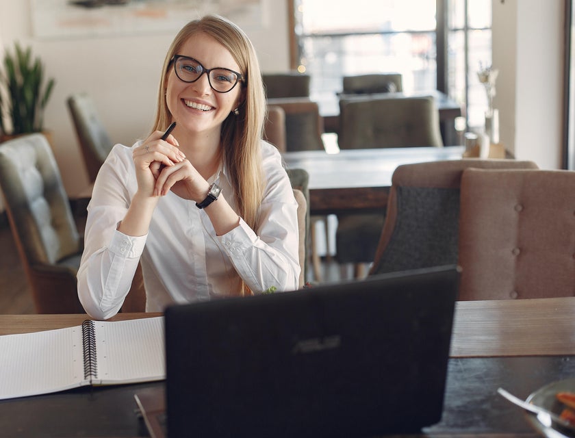 female Investment Banker wearing glasses while sitting in front of her open laptop and notebook