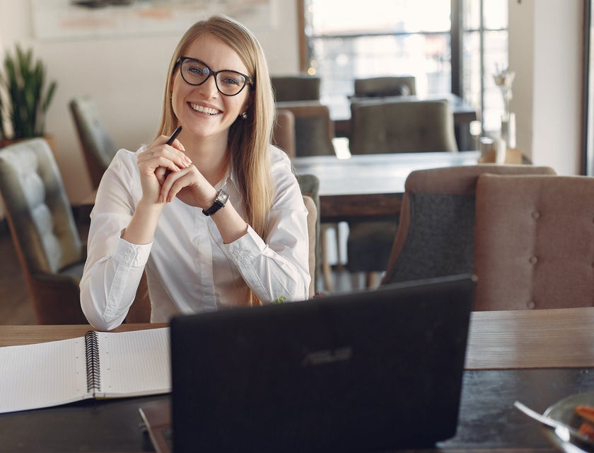 Investment Banker wearing glasses while sitting in front of her open laptop and notebook