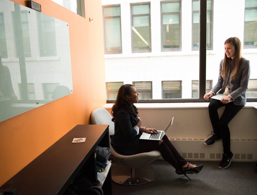female IT Support Specialist sitting on a chair with her laptop and having discussions with her colleague