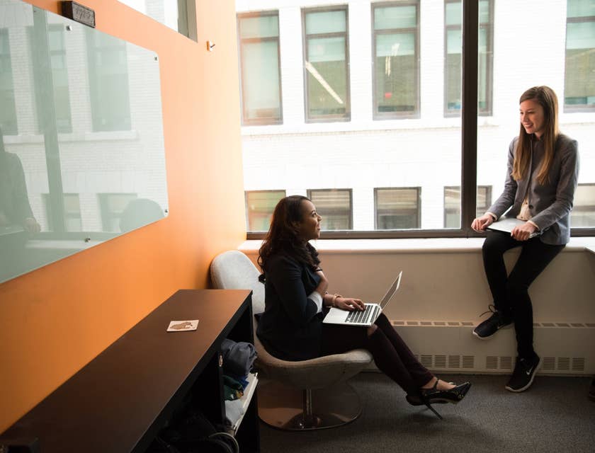 female IT Support Specialist sitting on a chair with her laptop and having discussions with her colleague