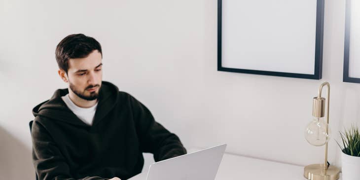 Java software engineer looking at the laptop with his mobile phone and a cup of coffee on the table.