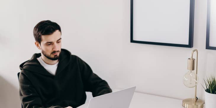 Java Software Engineer looking at the laptop with his mobile phone and a cup of coffee on the table