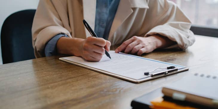 A woman in a beige coat filling out a job application form.