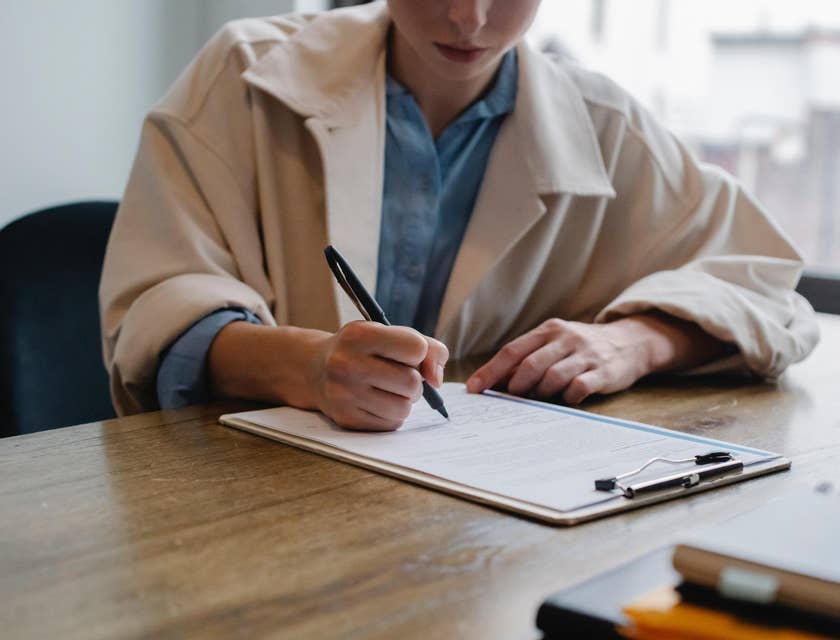 A woman in a beige coat filling out a job application form.