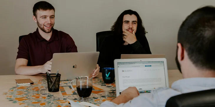 A junior web developer presenting his final web design with the rest of his team during a meeting.
