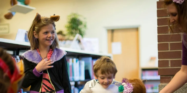 A kindergarten teacher assisting one of her students while wearing their costumes.
