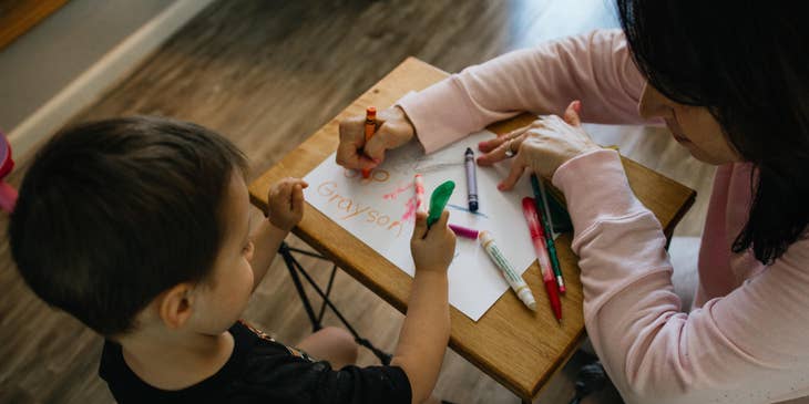 Lead toddler teacher helping a toddler with his drawing using crayons