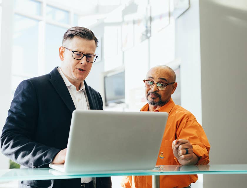 A life insurance agent in a black suit talking to a client in front of a laptop.