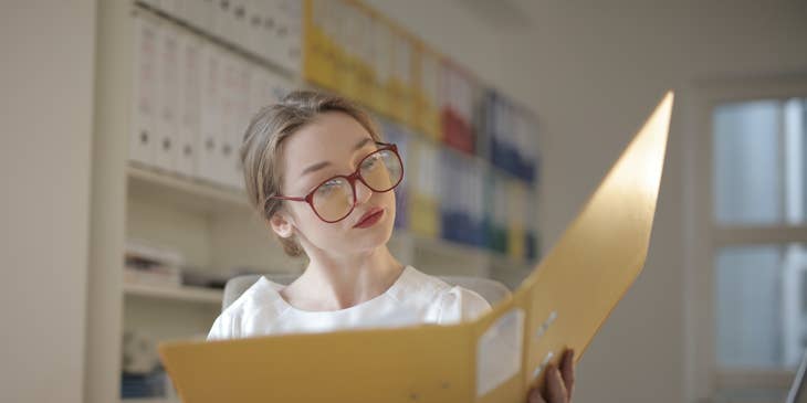 Female loan processor wearing eyeglasses looking at the documents within a yellow folder