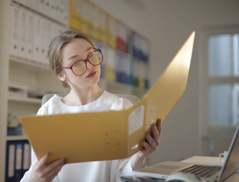Female loan processor wearing eyeglasses looking at the documents within a yellow folder