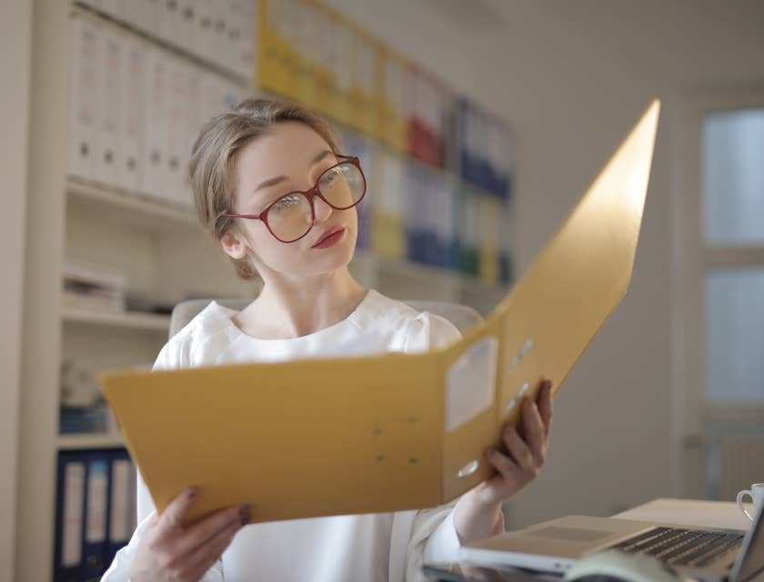 female loan processor wearing eyeglasses looking at the documents within a yellow folder