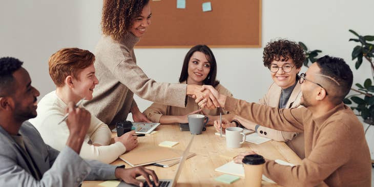 Loans consultant shaking hands with the team leader sitting beside his smiling colleagues