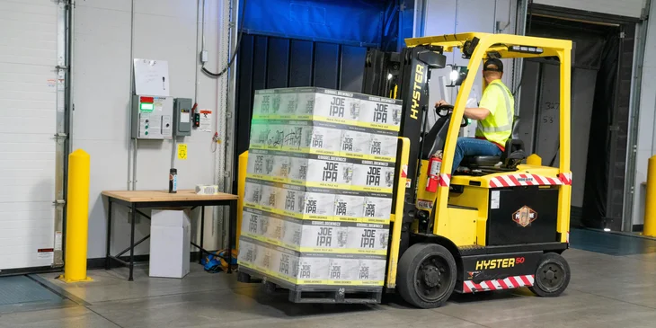 A longshoreman using a forklift in a warehouse loading cargos to be transported to the vessels.