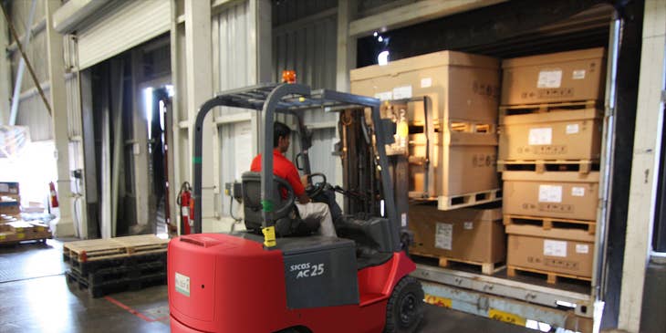 A longshoreman using a forklift in a warehouse loading cargos to be transported to the vessels.