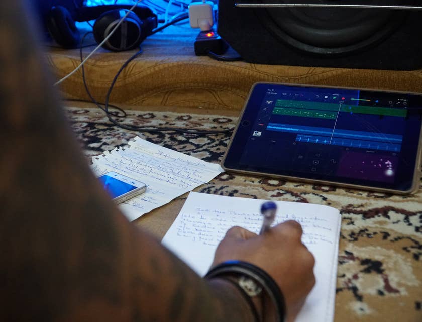 Lyricist writing lyrics on a notebook and pen and using a tablet playing a recording