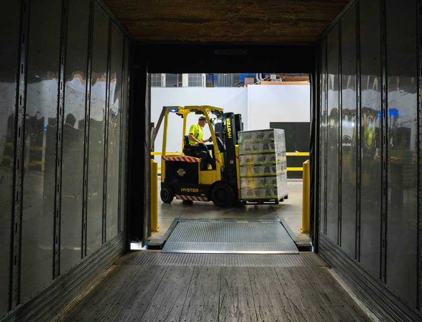 A material handler driving a forklift and about to transfer packages from the truck to the designated area inside the warehouse.