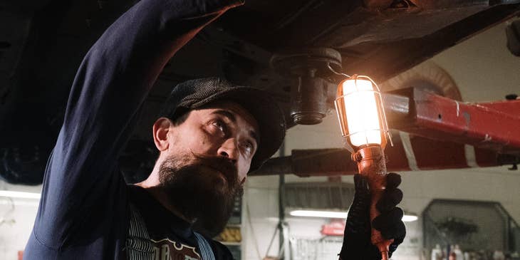 Mechanic holding a wrench and red light fixing a car.