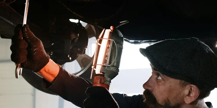 A mechanic holding a wrench and red light while fixing a car.