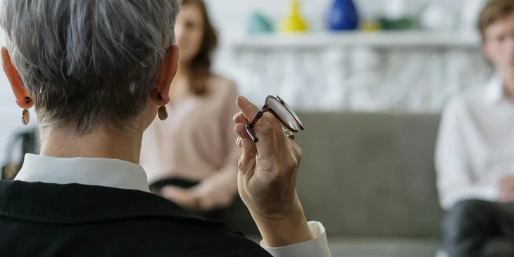 A mediator is holding her glasses as she listens to a client's conflict.