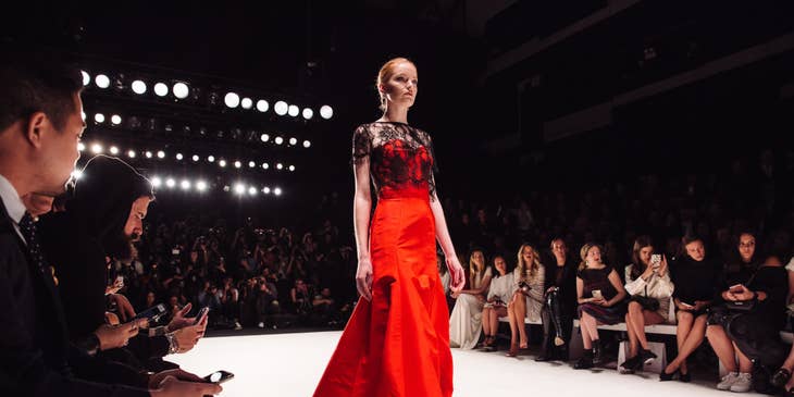 A model wearing a red gown walking on a catwalk for a year-end fashion show.
