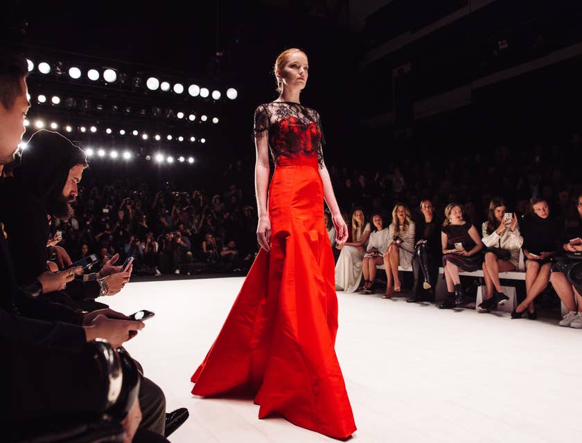 A model wearing a red gown walking on a catwalk for a year-end fashion show.