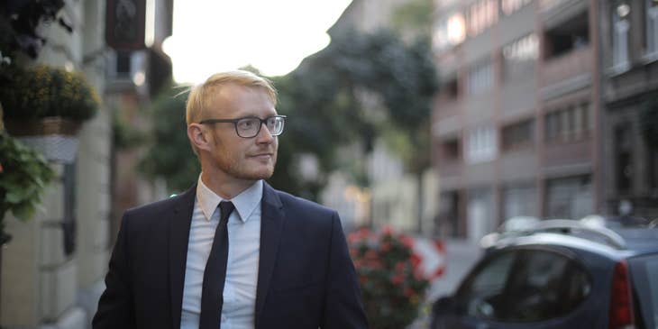 Male mortgage closer wearing a business suit looking sideways with houses and buildings lining the street behind him.
