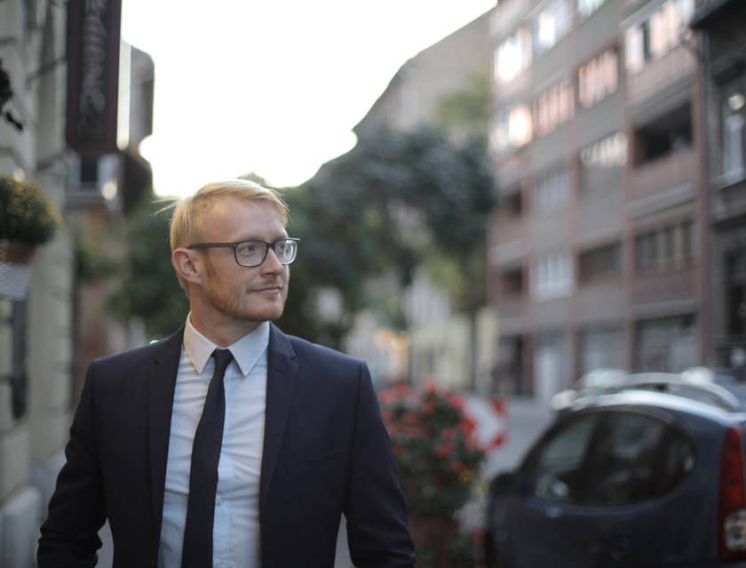 Male mortgage closer wearing a business suit looking sideways with houses and buildings lining the street behind him.