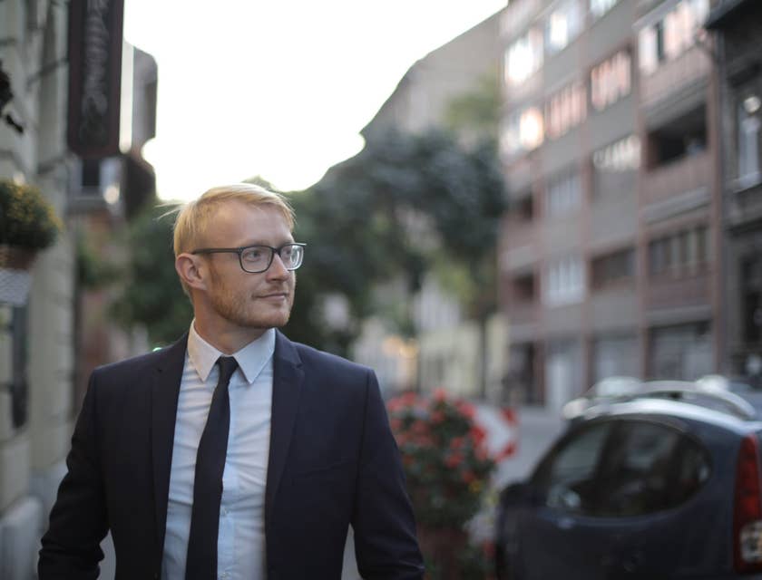 male mortgage closer wearing a business suit looking sideways with houses and buildings lining the street behind him