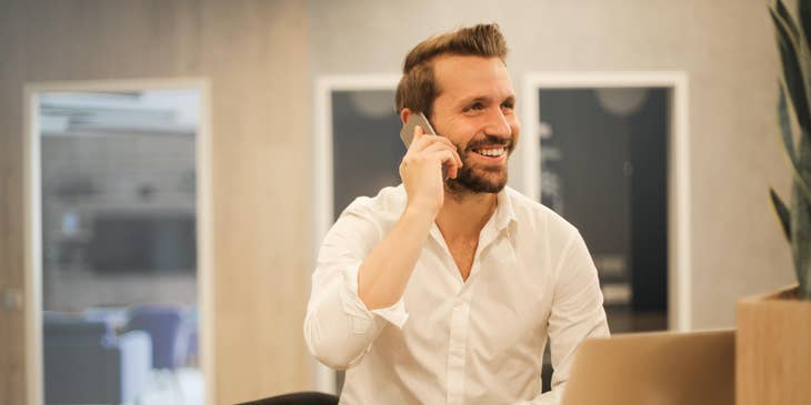 Mortgage underwriter using his mobile phone while sitting in front of his open laptop